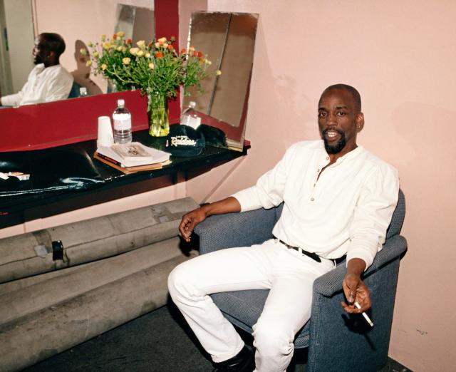 Man wearing an all white outfit sitting in a chair holding a cigarette.